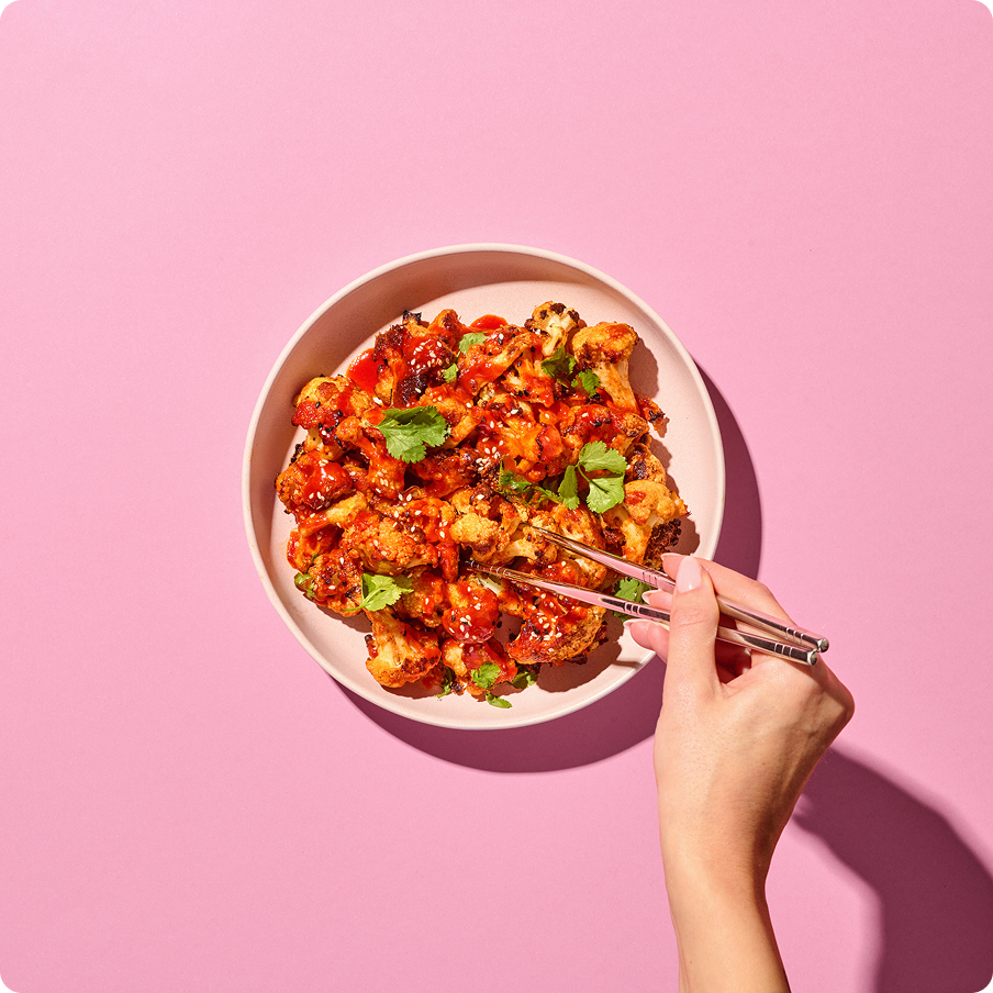 Gochujang-Blumenkohl-Wings in einer Schale und eine Hand hält Essstäbchen darein