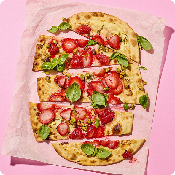 Ein Flammkuchen mit Erdbeeren und Basilikumblättern, der in Stücke geschnitten ist und auf einem Backpapier liegt